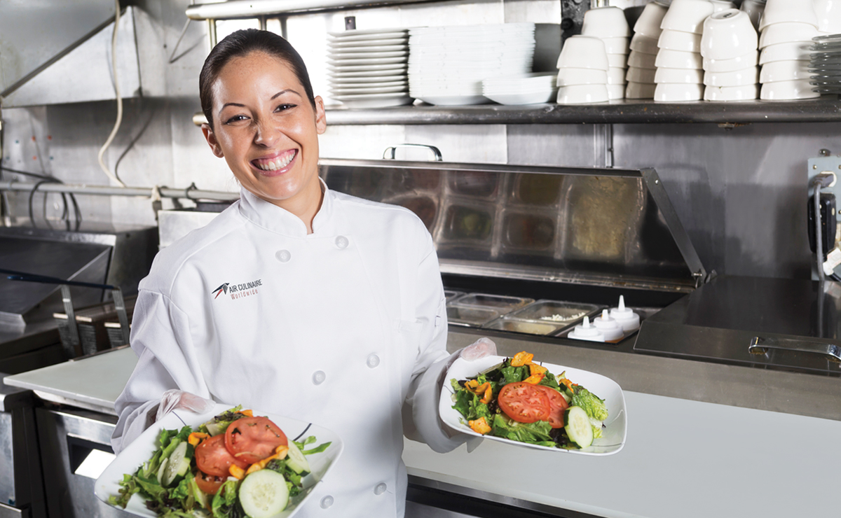 Chef holding two salad plates standing in the kitchen smiling