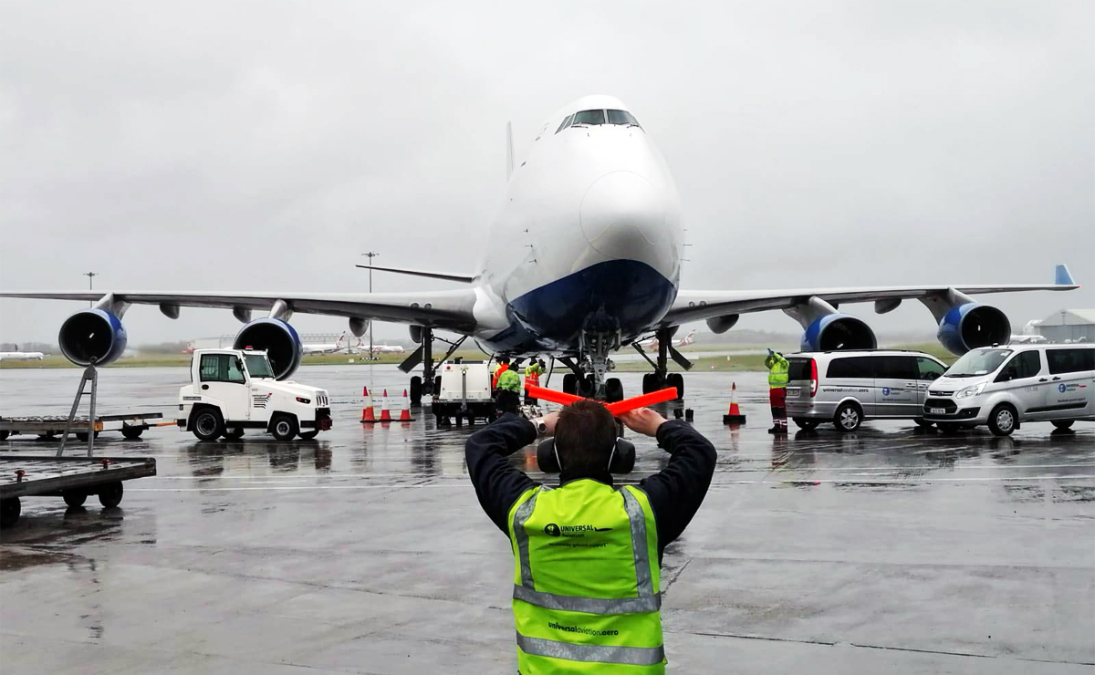 An air marshaller in Universal Aviation vest standing in front of an aircraft raising his hands